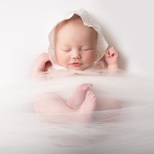 Newborn girl wearing a lace bonnet on a white background, timeless and delicate portrait
