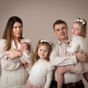 Family of five with mum, dad, and three daughters posing on a cream background during a family portrait session