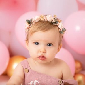 girl wearing a pink hairband in a birthday-themed photoshoot with balloons