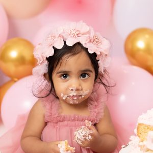Cake smash photography session for a 1st birthday celebration with a baby enjoying their birthday cake.