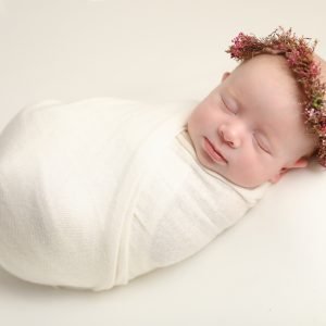 Newborn baby girl wrapped in a soft cream wrap on a matching cream backdrop