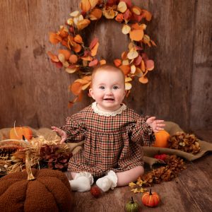 Red-haired girl in an autumn mini session with a rustic background and orange pumpkins