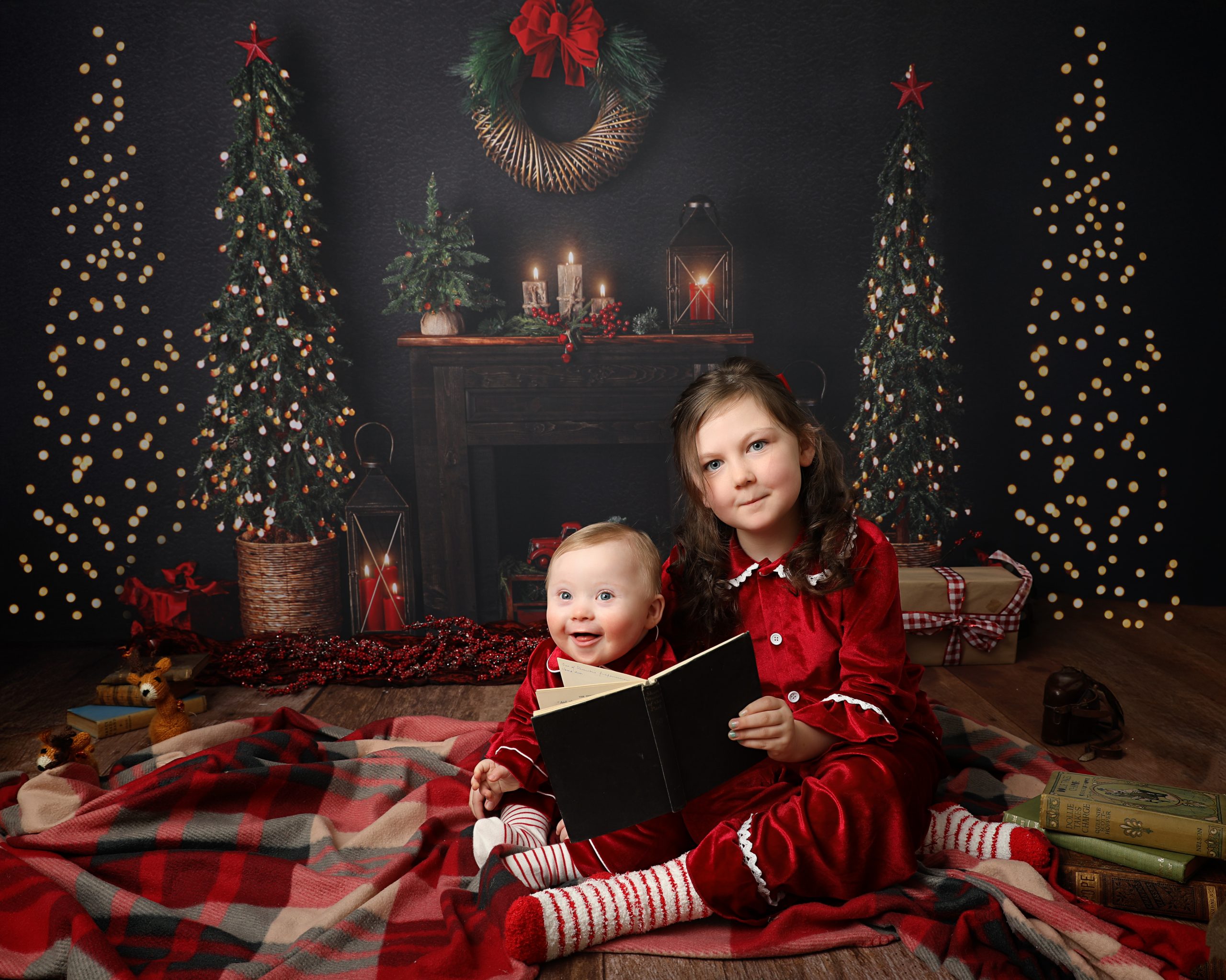 Brother and sister reading a book during a Christmas Mini session surrounded by Christmas trees and sparkly lights at Daisy May Photography