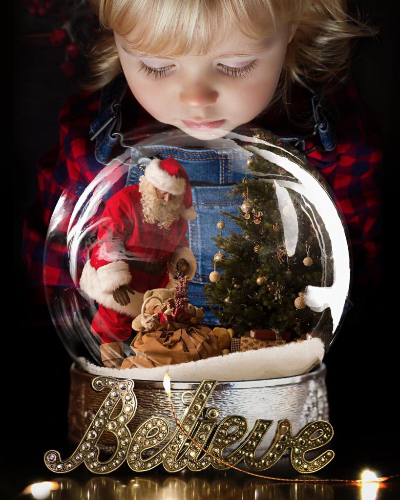 Boy looking into a snow globe with Santa Claus during a Christmas Mini session at Daisy May Photography.